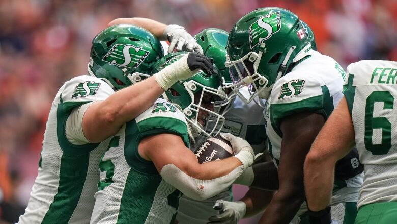 A group of football players wearing white and green jerseys huddle and celebrate.