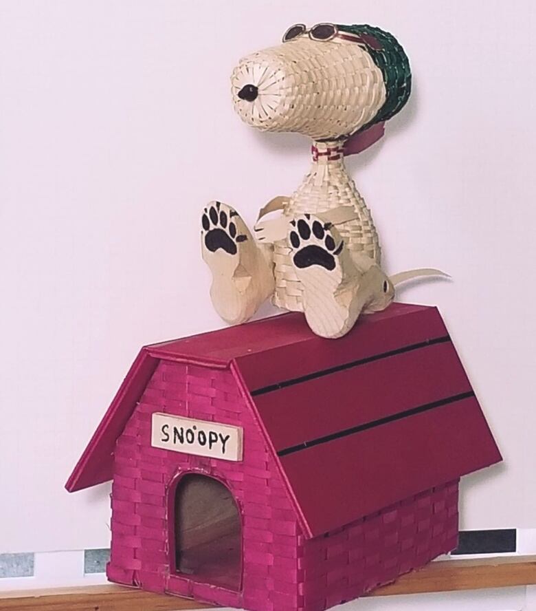 A sculpture of Peanuts character Snoopy sitting on the roof of his red dog house.