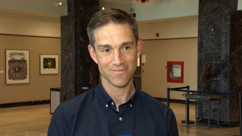 A smiling man wearing a blue shirt stands in the lobby of Confederation Building.