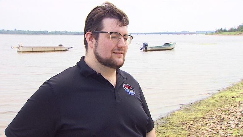 Man standing on shore with two boats in background.