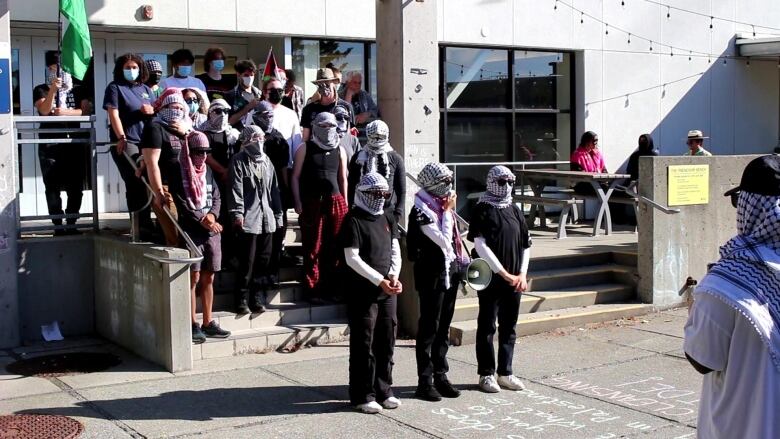 A group of people, mostly women, stand on the steps with their eyes and faces covered.