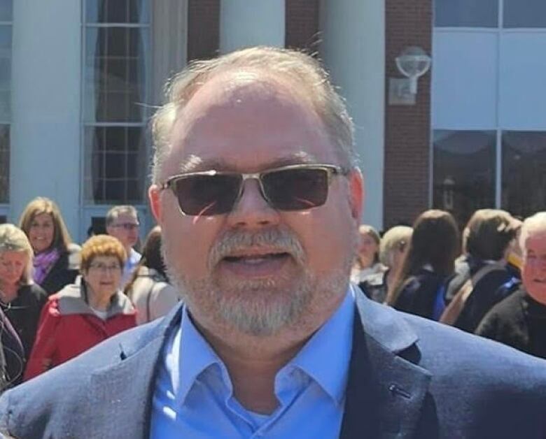 A smiling man in a blue blazer and sunglasses.