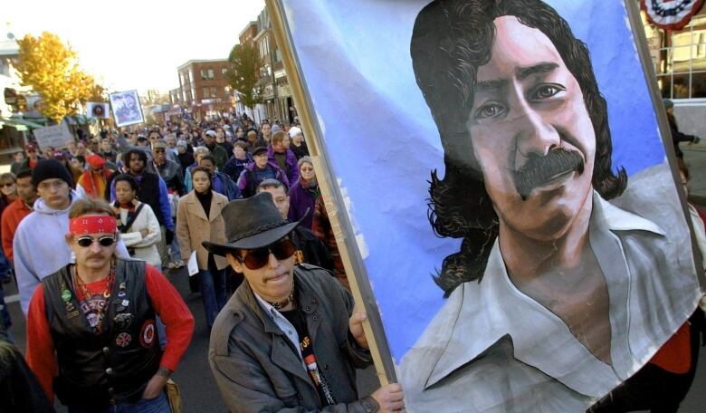 Ralliers march in the streets, some holding a large painting of Leonard Peltier.