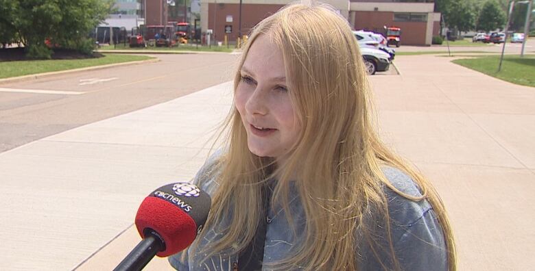 Teenaged girl with long blonde hair in front of a brick school building. 