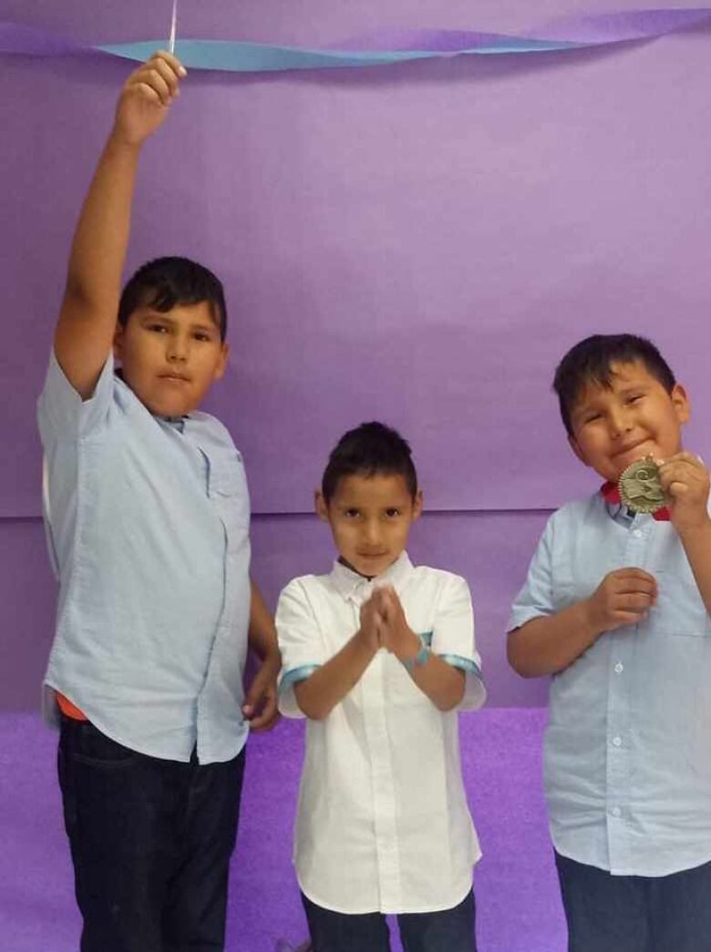 Three children stand in front of a purple background.