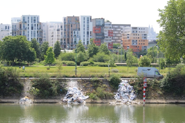 Garbage bags are visible on the edge of a large river in a city.