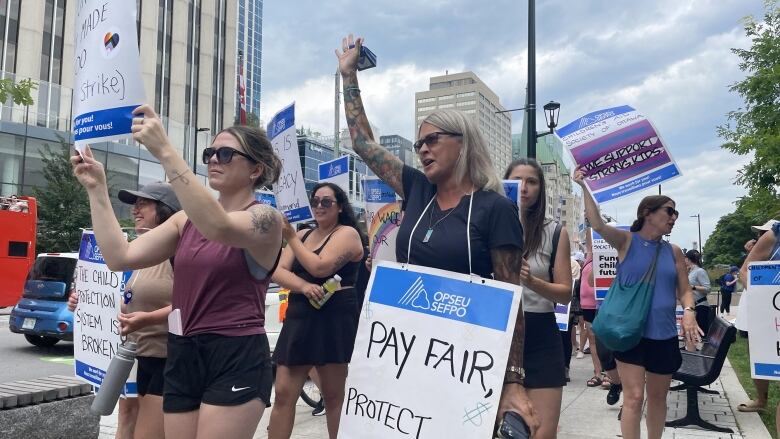 A group of workers walk down a sidewalk holding signs and chanting. 