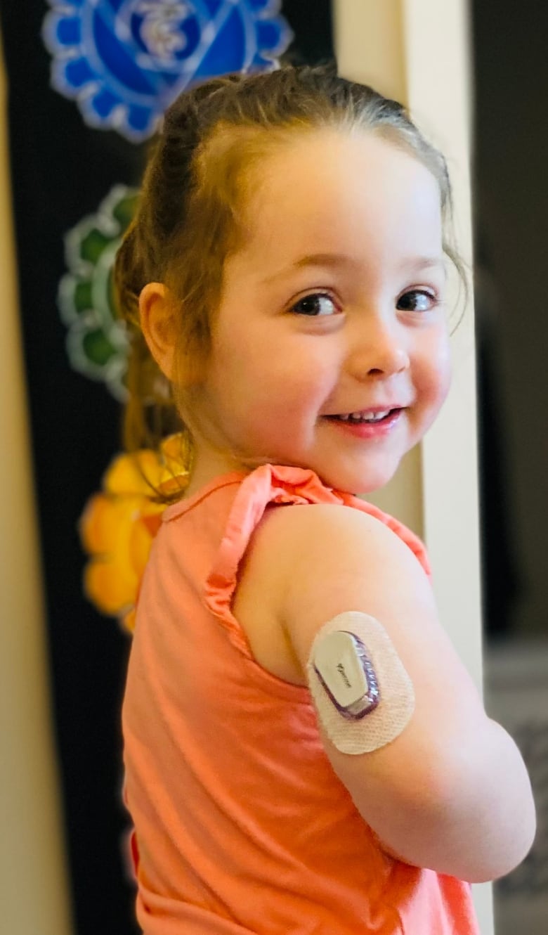 A girl in a pink shirt with a device on her arm and lower back. 