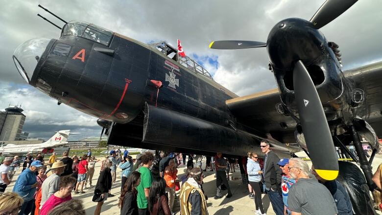 A crowd of people is shown looking at large black vintage airplane on a tarmac.