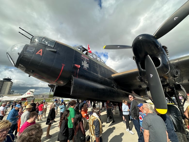 A crowd of people is shown looking at large black vintage airplane on a tarmac.