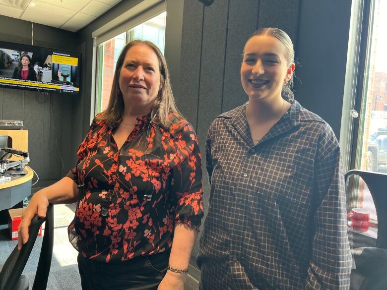 A middle aged woman and high school aged girl pose side by side for a photo in a radio studio