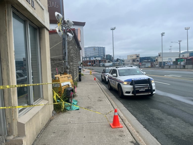 Two police cars are parked in front of a building.. The entrance is covered with police tape.