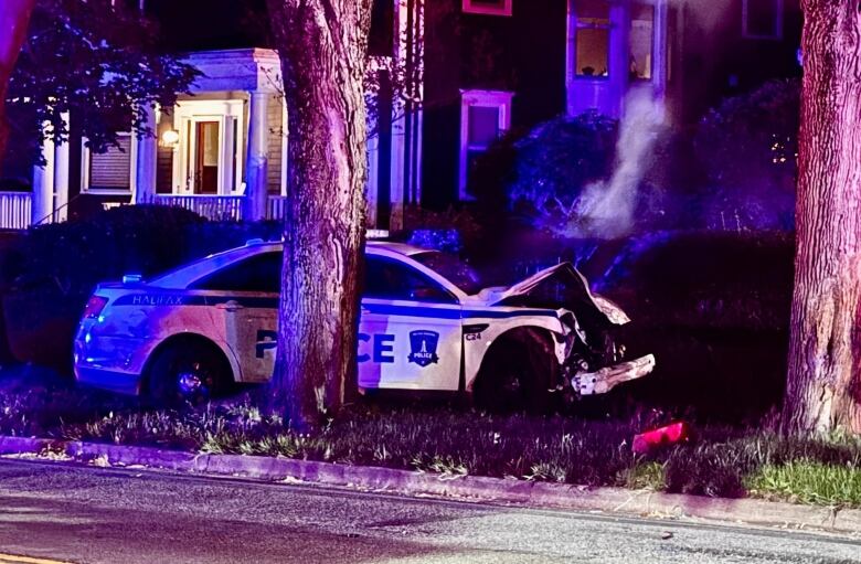 A police car with a smashed front behind a large tree