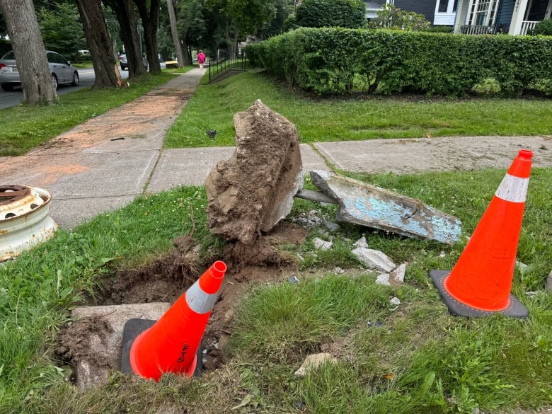 An upended concrete street knocked onto its side on a patch of grass. The marker is surrounded by two neon orange pylons.