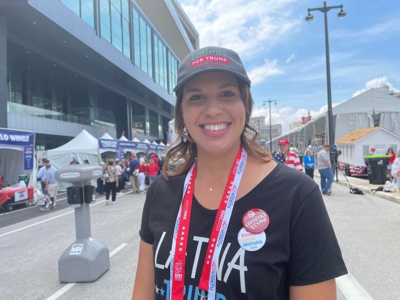 A young woman wears a Latinos for Trump hat and several lanyards.