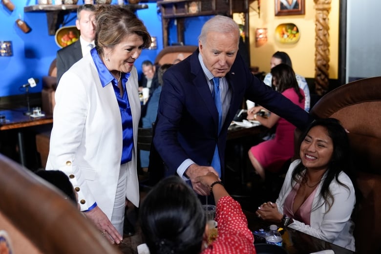 A person standing shakes hands with diners seated at a table.