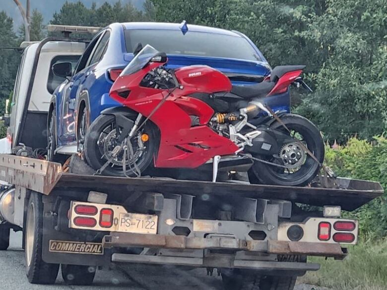 A red motorbike and a blue car are seen in the back of a truck.