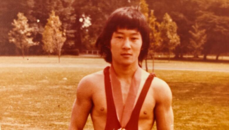 A person in a wresling singlet and a medal stands in a park.