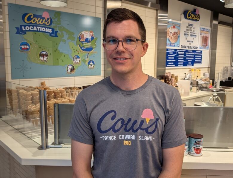 A man with glasses and short hear wears a grey t-shirt at smiles at the camera. 