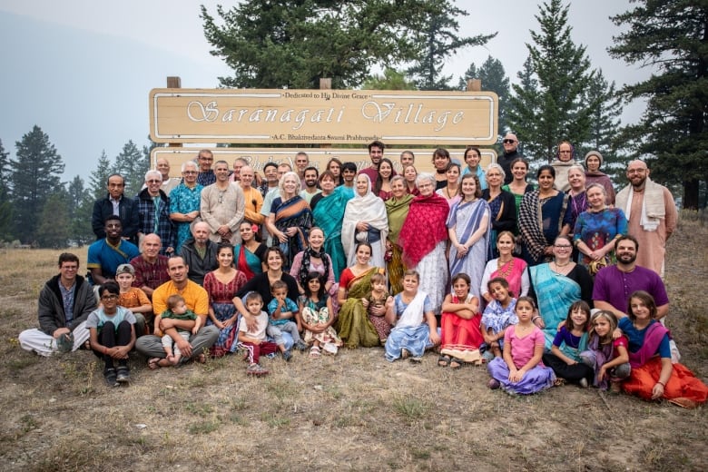 A group photo of families outside a sign that reads 'Saranagati Village.'