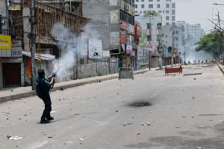 A police officer fires tear gas on a street with debris.