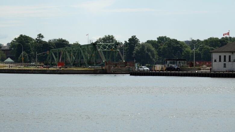 A wide photo of a piece of a green, metal bridge resting next to open water and a beige brick building.