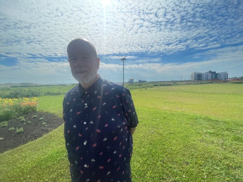 A man stands on a grassy lawn with an osprey platform behind him 