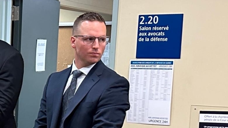 A man in a suit stands in a courtroom