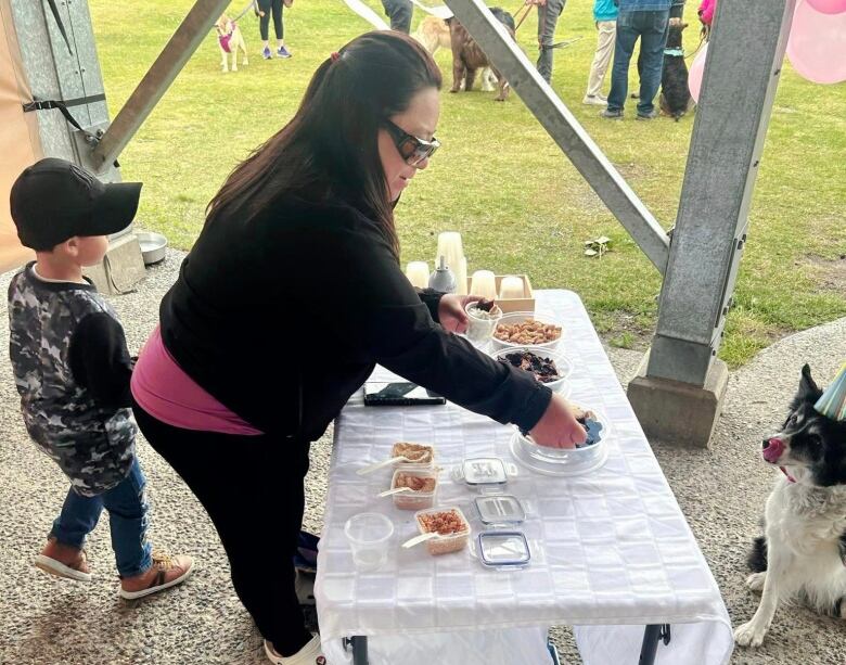 a woman stands behind a table of treats while a dog waits patiently