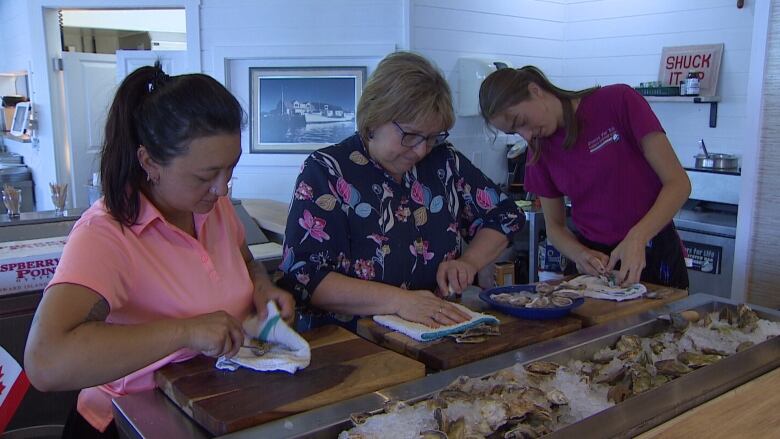 Three women shucking oysters.