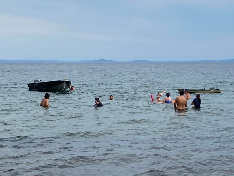 Wide shot of several people in water near boats 