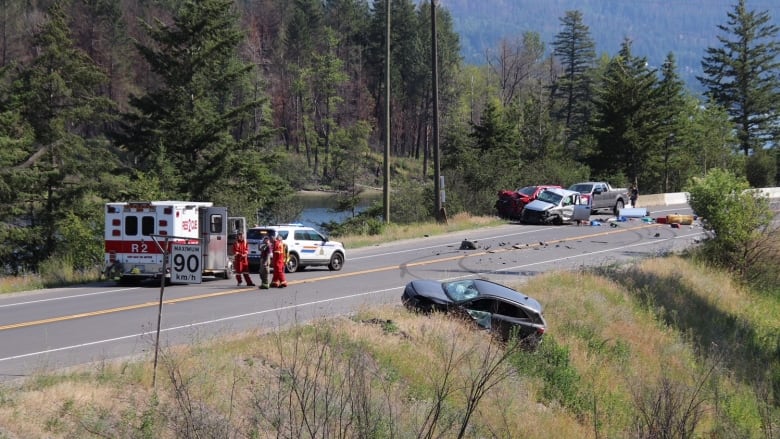 A scene of multiple vehicle crash at a highway with paramedics and an ambulance responding. 