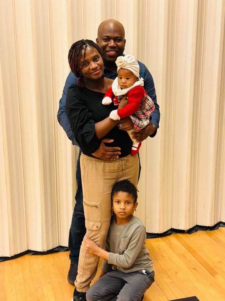 A Black wife and husband embrace while holding their two young children. 