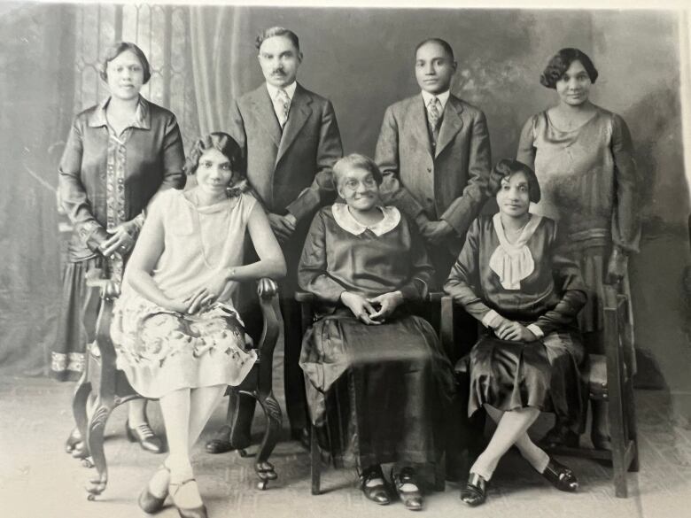 An old black and white group portrait, with four people standing behind three other adults who are sitting in chairs.