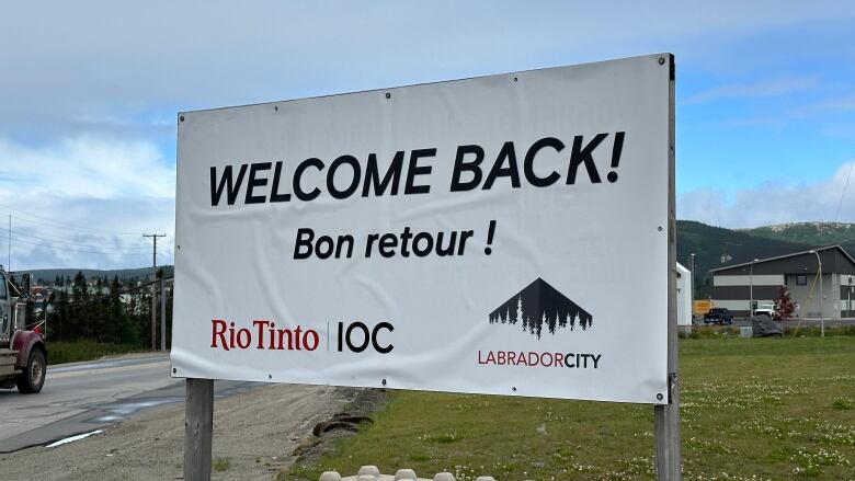 A white sign reads 'Welcome Back!' and 'Bon Retour!' in black lettering. The sign has logos for Riotinto IOC and the town of Labrador City on it.