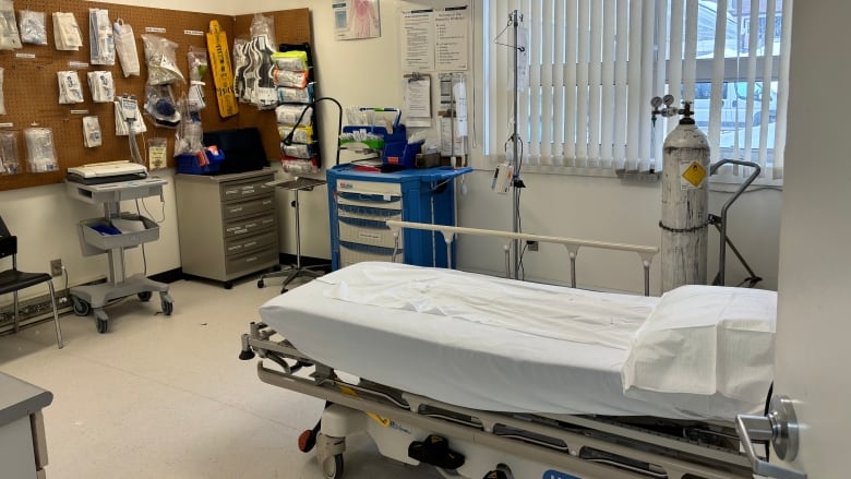 A hospital room with a bed, oxygen tank and carts of supplies is shown.