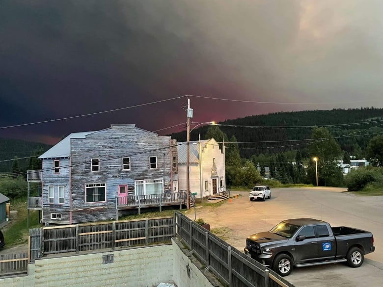 Light and smoke from a wildfire form over wooden buildings.