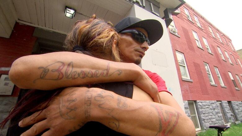 A man and women hug each other outside on the steps of an apartment building. 