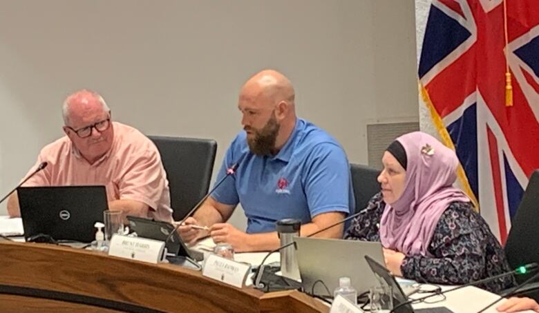 Woman, wearing pink hijab, sitting at a table, speaking into microphone.