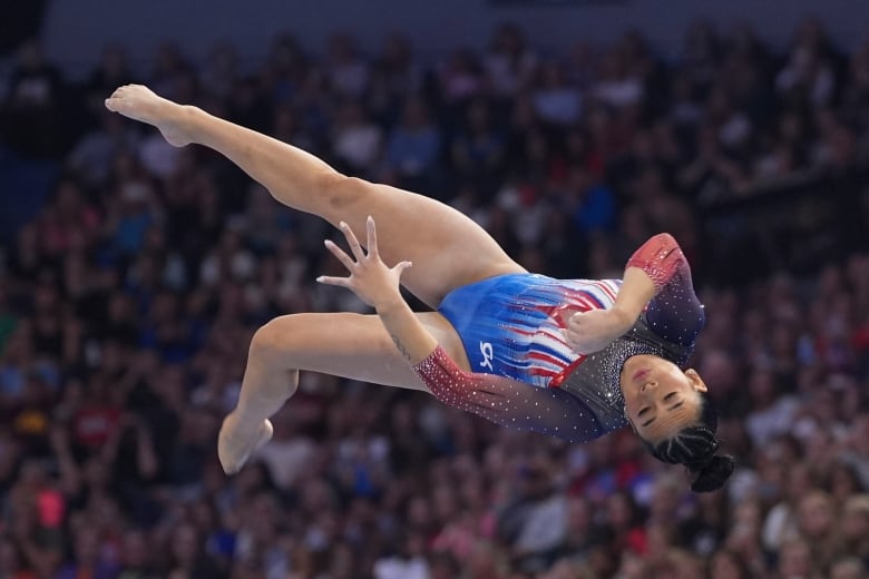 A woman in a gymnastics  leotard flips through the air