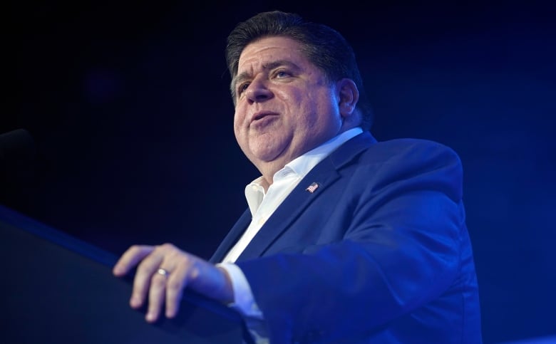 Heavy-set white man in suit with no tie speaking on a podium.