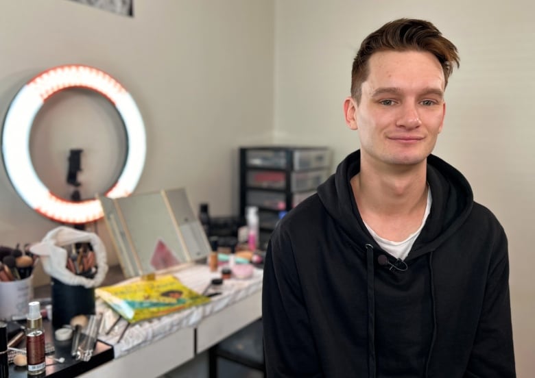 Medium shot of young man, makeup table in the background