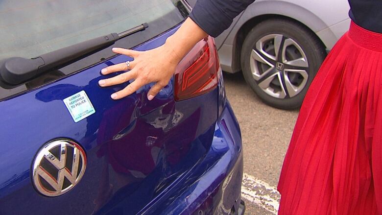 Woman pointing out damage to blue car.