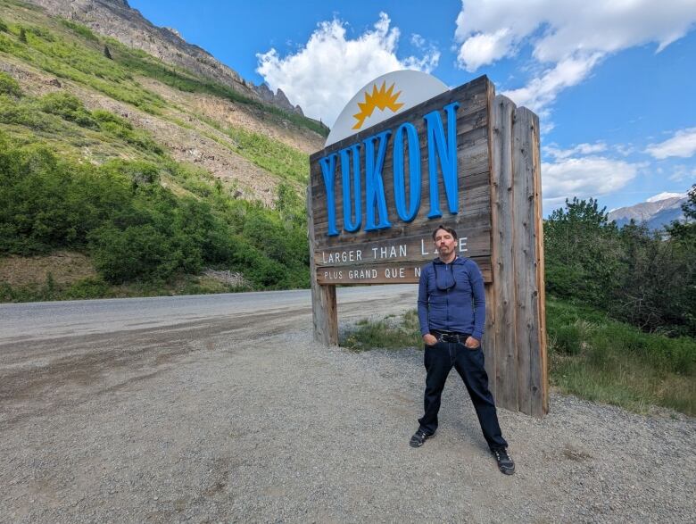 A man poses with a Yukon sign. 