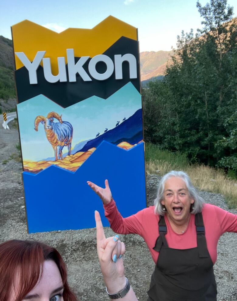 A woman raises her arms in front of a Yukon sign 