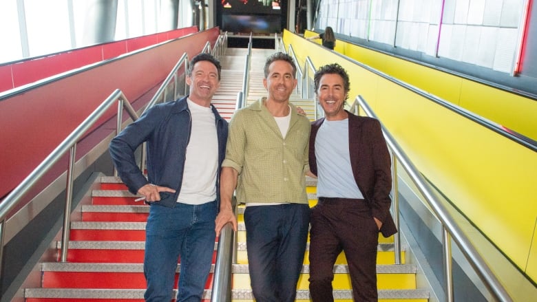 Three men pose on a staircase that is painted red and yellow.