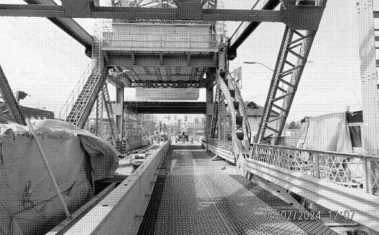 A black and white photo looking along a bridge shows a support on the right side with a big bend in it.