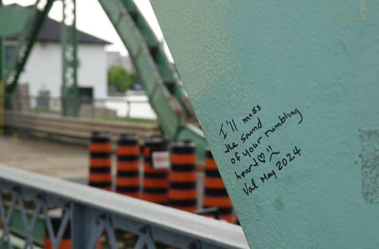 A handwritten message in permanent marker includes a heart and a sad face. In the background two, bent pieces of metal can be seen.