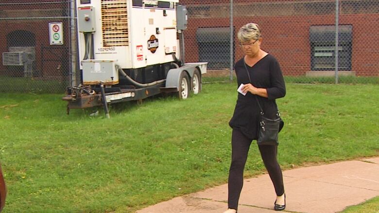 Woman dressed in black walking along sidewalk.