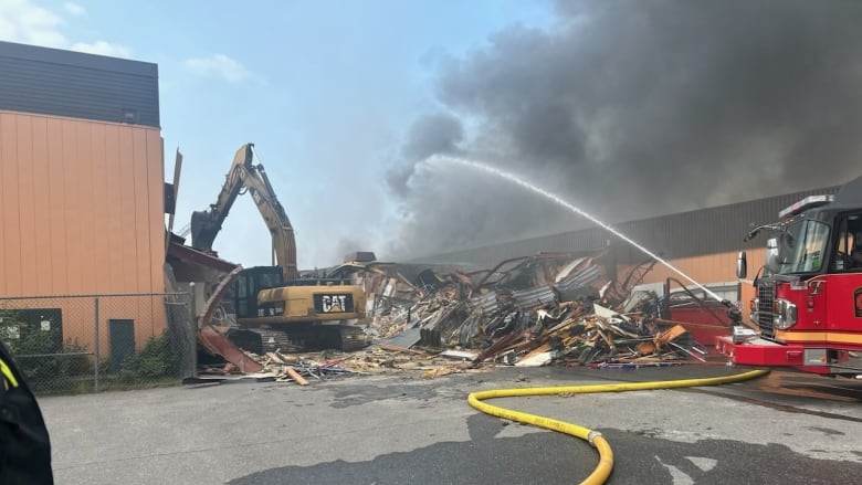 A fire truck sprays water on smoking rubble beside a large building.